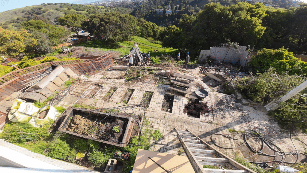 All Access Construction before photo of failed hillside retaining wall in Belmont, showing collapsed blocks, debris, and slope failure before new concrete wall, piers, and grade beam rebuild.