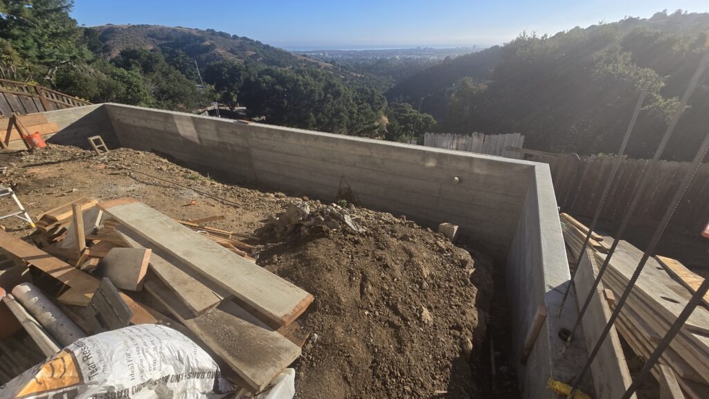 All Access Construction showing finished retaining wall and grade beam on Belmont hillside with open work area before backfill.
