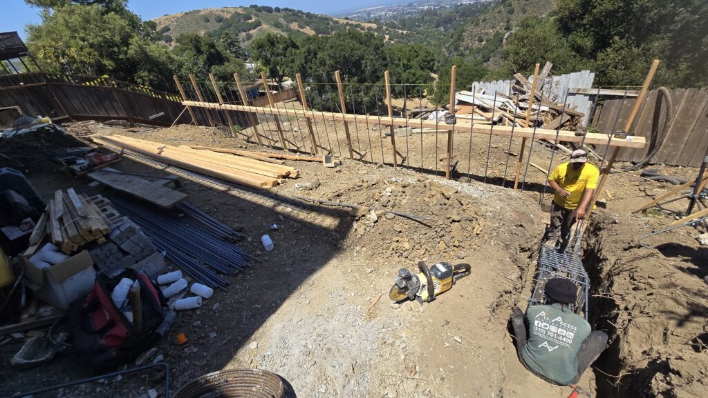 All Access Construction crew installing rebar cage for concrete pier during retaining wall rebuild in Belmont, San Mateo County, hillside excavation in progress.
