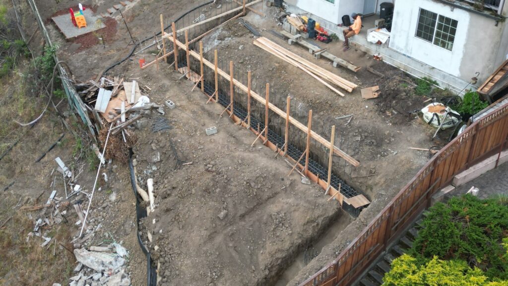 All Access Construction drone view of trench excavation and rebar installation for 75-ft Belmont retaining wall with grade beam and concrete piers.