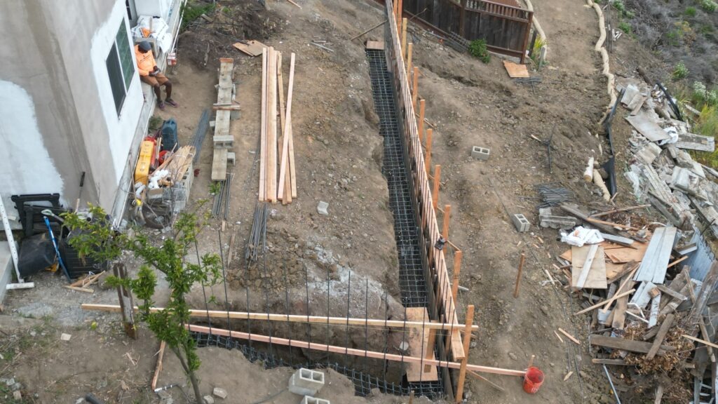 All Access Construction drone view of retaining wall grade beam trench with rebar cages installed for concrete pour in Belmont.