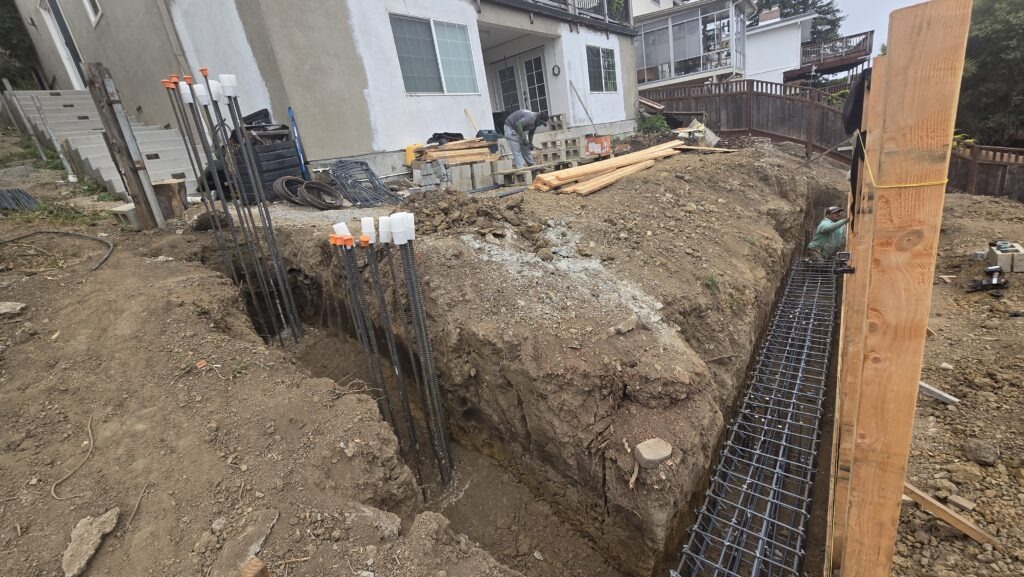 All Access Construction close-up of grade beam excavation with vertical bars and rebar cage set for Belmont retaining wall project.