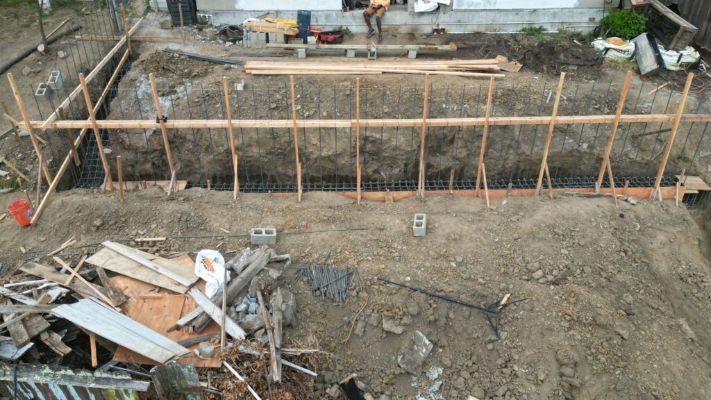 All Access Construction crew installing formwork for concrete retaining wall along steep Belmont hillside with vertical rebar in place.