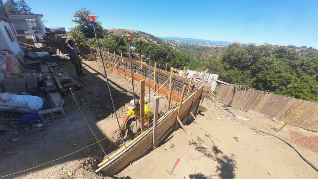 All Access Construction drone overhead view of concrete retaining wall pour and grade beam in Belmont hillside property.