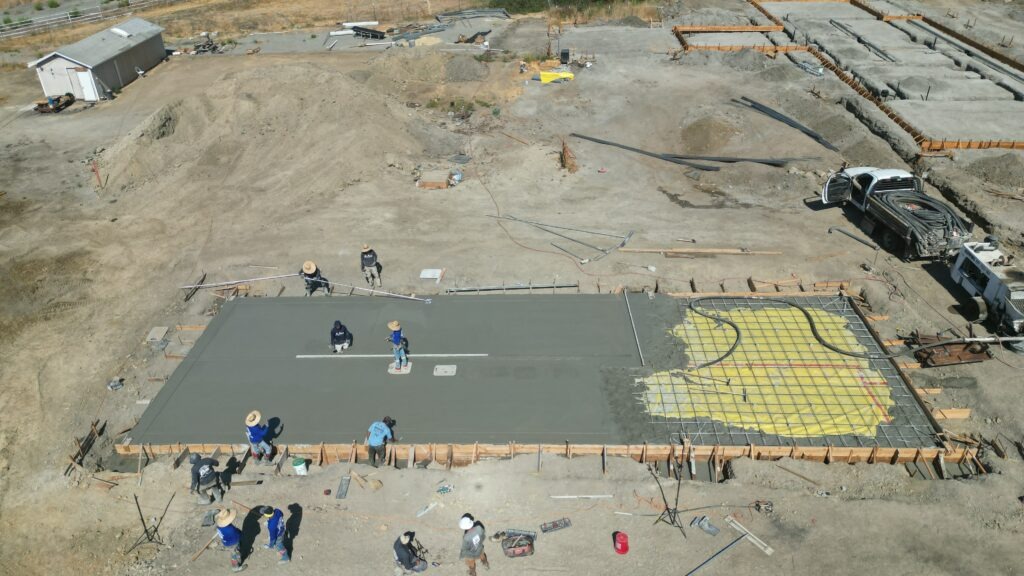 Drone shot of All Access Construction pouring and leveling concrete for the Milpitas carport slab with finishers working the surface.