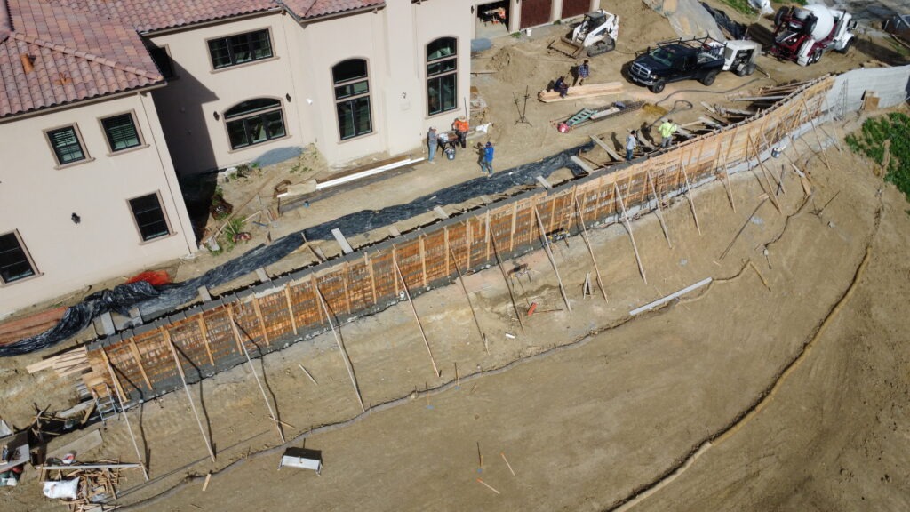 Drone view of long concrete retaining wall under construction with forming and bracing in Milpitas