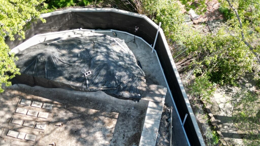 Aerial shot of curved concrete retaining wall rebuild in Walnut Creek, showing drainage pipe layout and excavation work