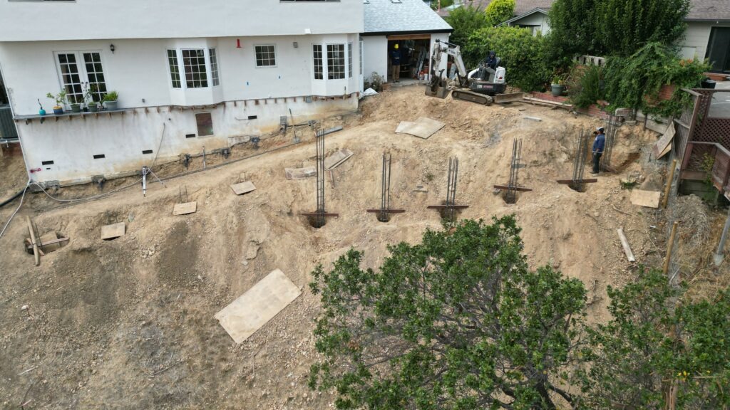 All Access Construction drilling deep concrete piers on a steep San Rafael hillside for a structural retaining wall, showing rebar cages, excavation challenges, and tight access conditions.