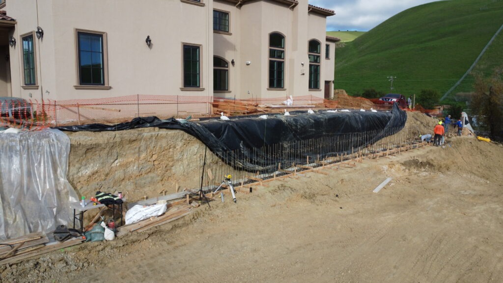 Wide drone view of concrete grade beam installation at hillside property in Milpitas CA near San Jose
