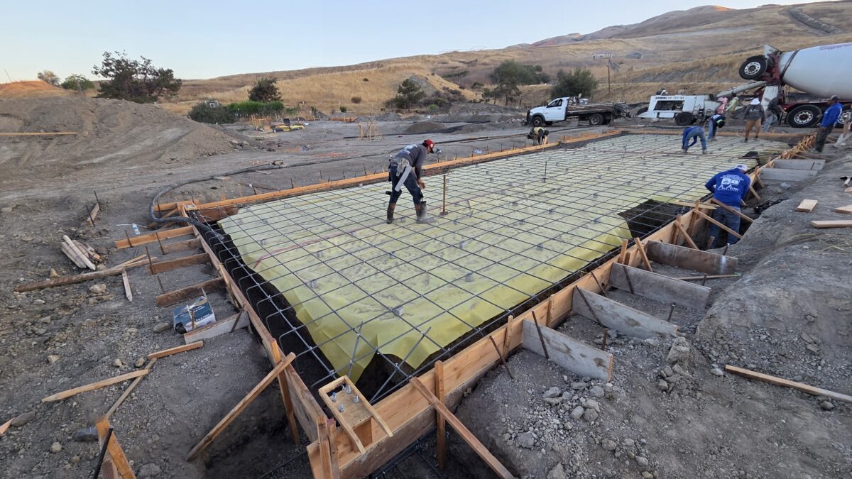 Drone overhead of concrete trucks and crew pouring Milpitas carport foundation slab.