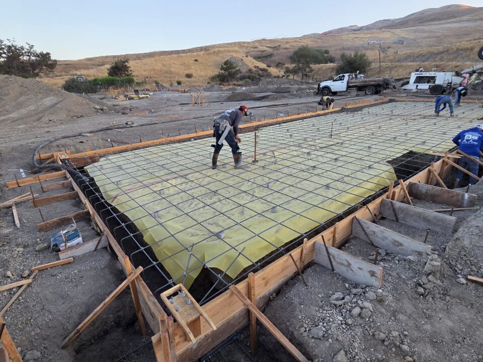 Drone overhead of concrete trucks and crew pouring Milpitas carport foundation slab.